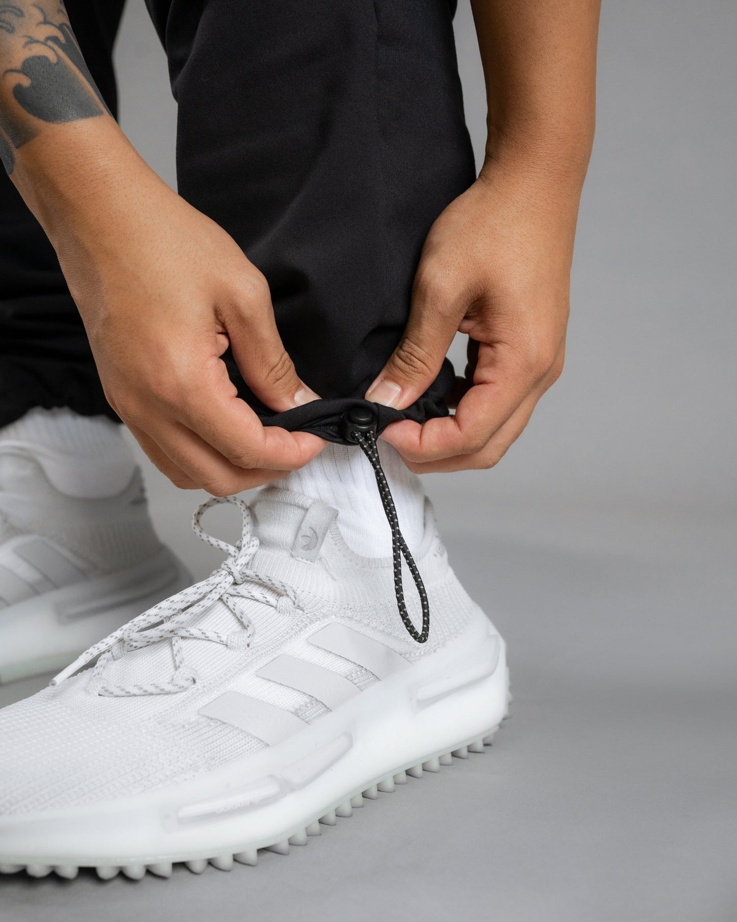 Close up of shoe and bottom of pant leg. Model highlighting the interior black and white striped pull cord with minimal round stopper of the SUPERNATURAL II JOGGER - ALL IN ALL