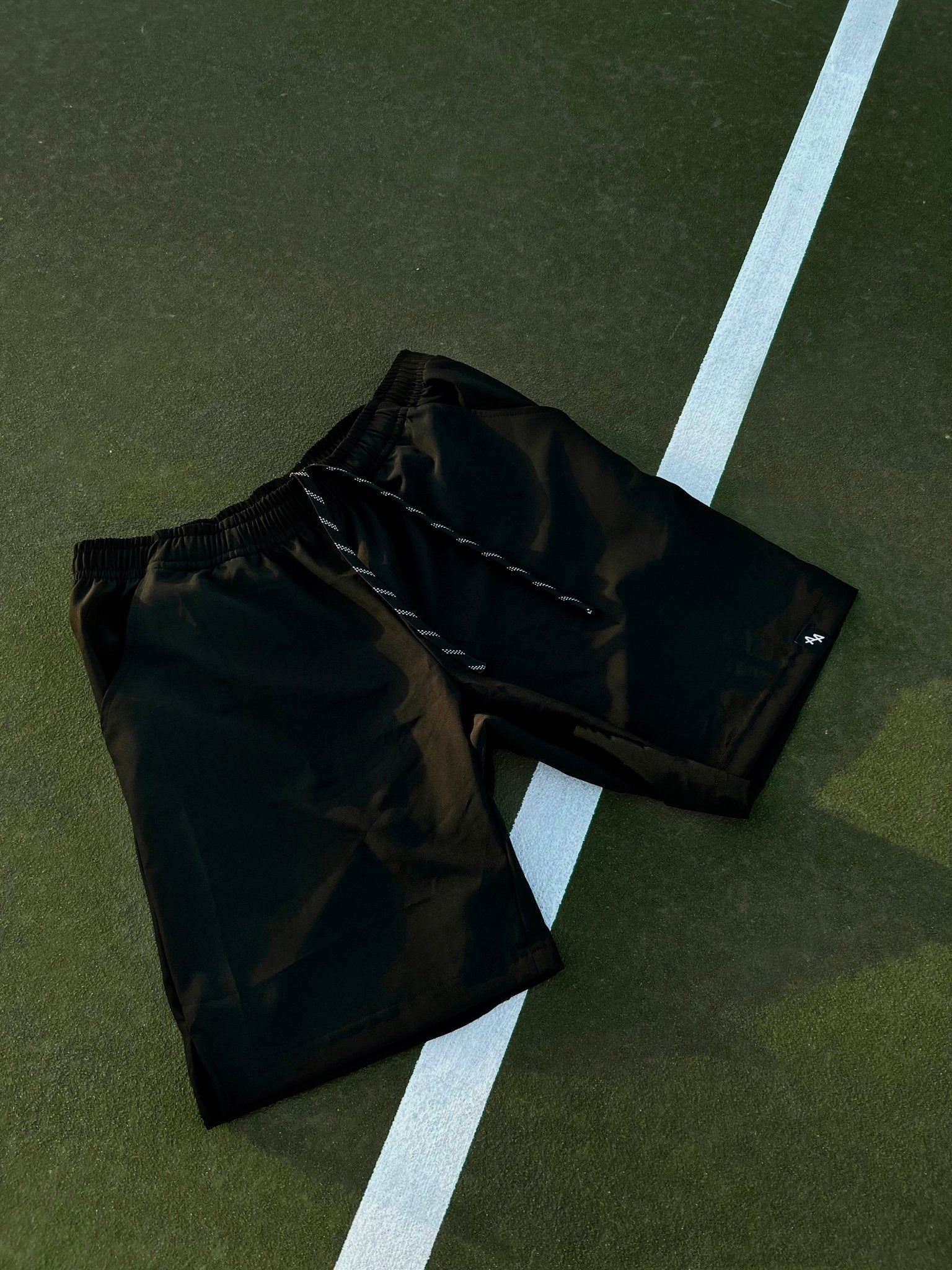 Dramatic shot of the ALL IN ALL black supernatural shorts overlayed on a green tennis court with white court lines