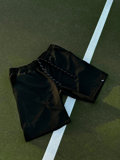 Dramatic shot of the ALL IN ALL black supernatural shorts overlayed on a green tennis court with white court lines