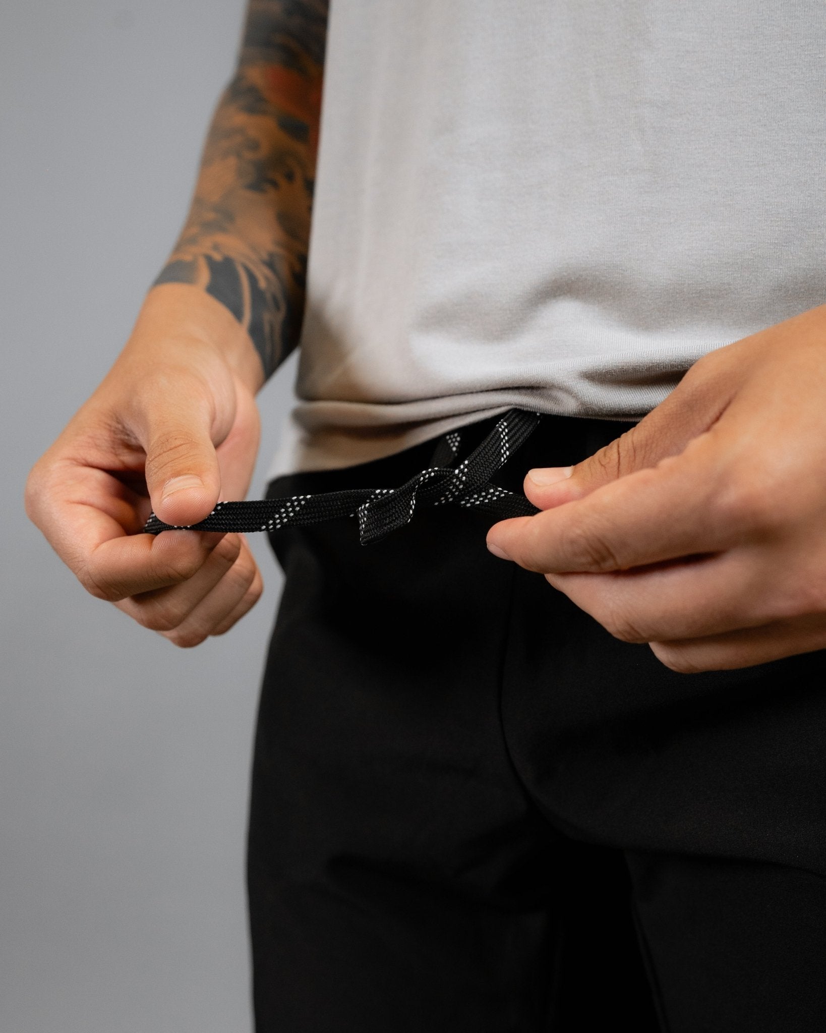 close up of model wearing the ALL IN ALL black supernatural short showcasing the black and white striped interior drawcord pulled out while model is tying the cord