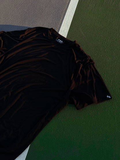 dramatic photo of ALL IN ALL black supernatural tee laying on top of green and grey tennis court with white court lines