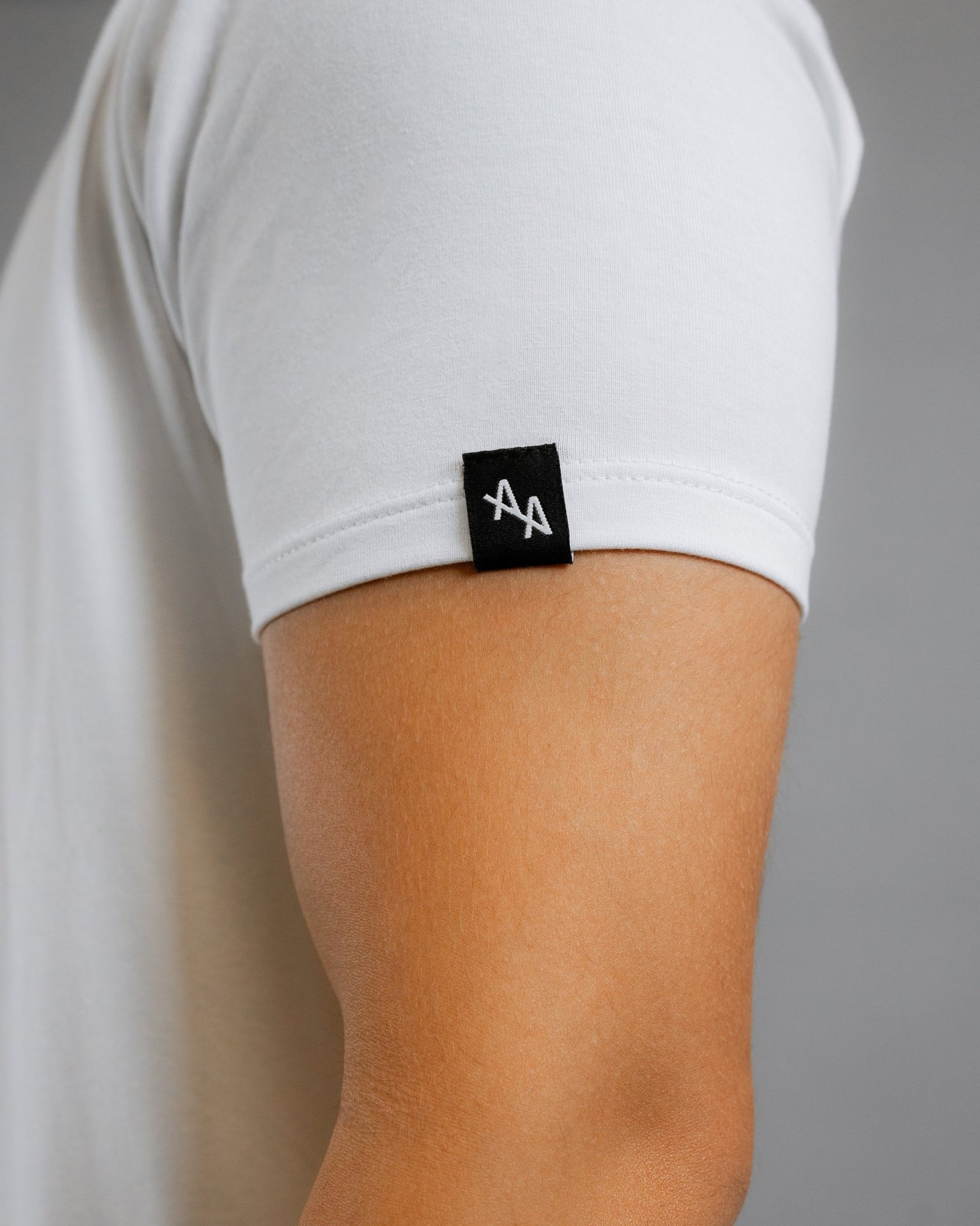 close up of ALL IN ALL off-white supernatural tee left sleeve focusing on sewn on black woven label featuring white double "A" ALL IN ALL logo