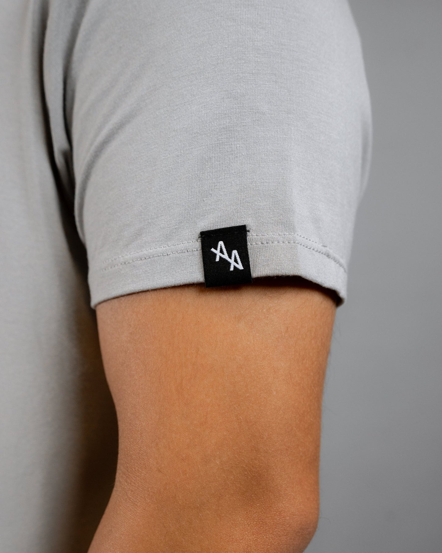 close up of ALL IN ALL sand supernatural tee left sleeve featuring sewn on black woven label with white double "A" ALL IN ALL logo