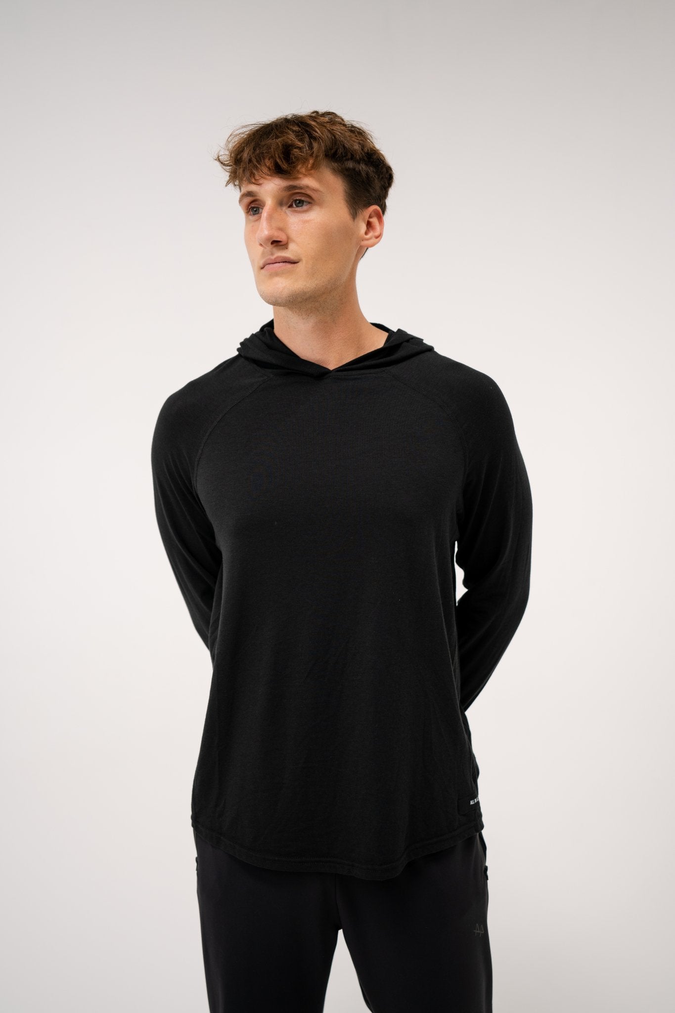 Male model wearing an ALL IN ALL black hoodie against a plain background