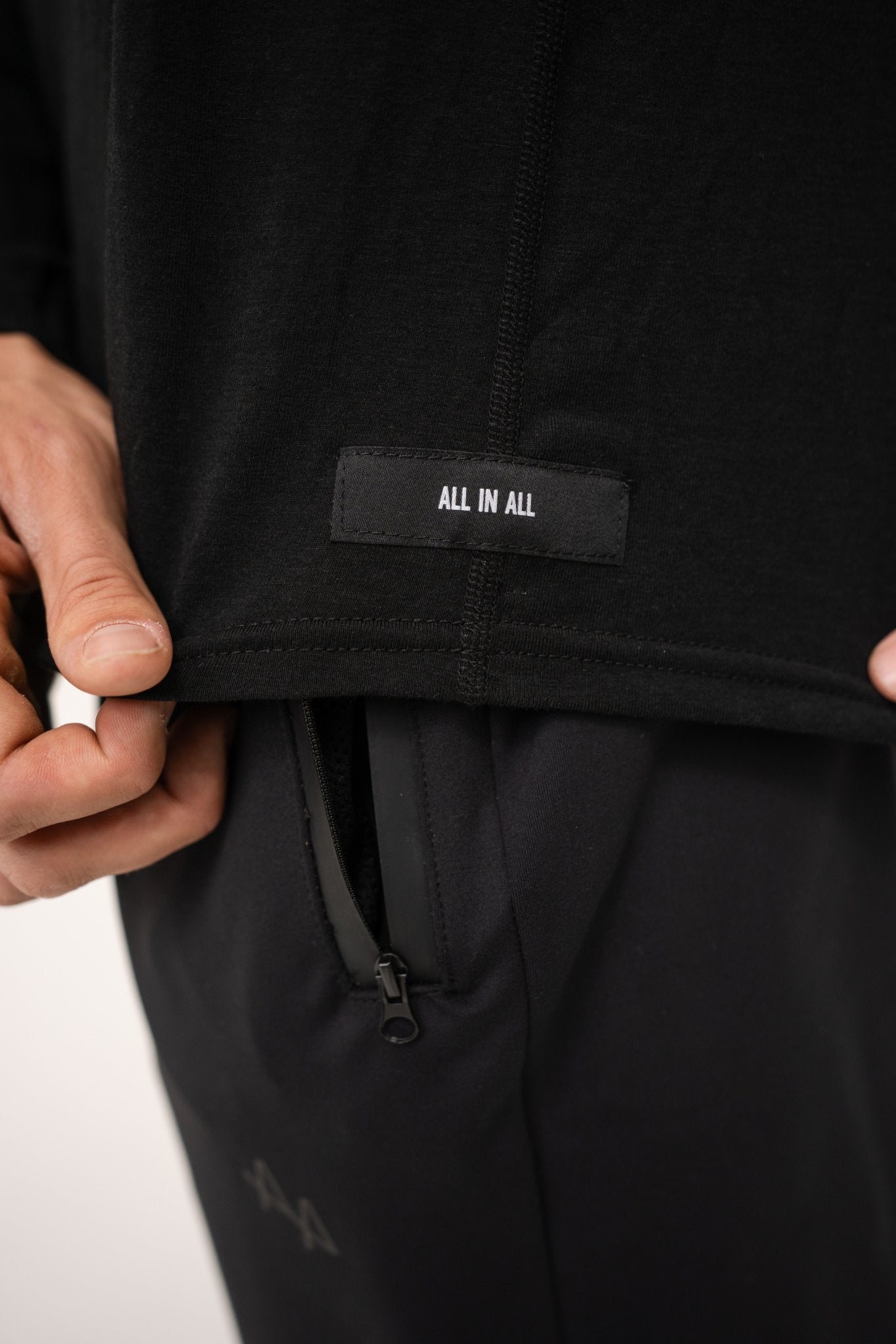 Close-up of ALL IN ALL black hoodie with black 'ALL IN ALL' label 