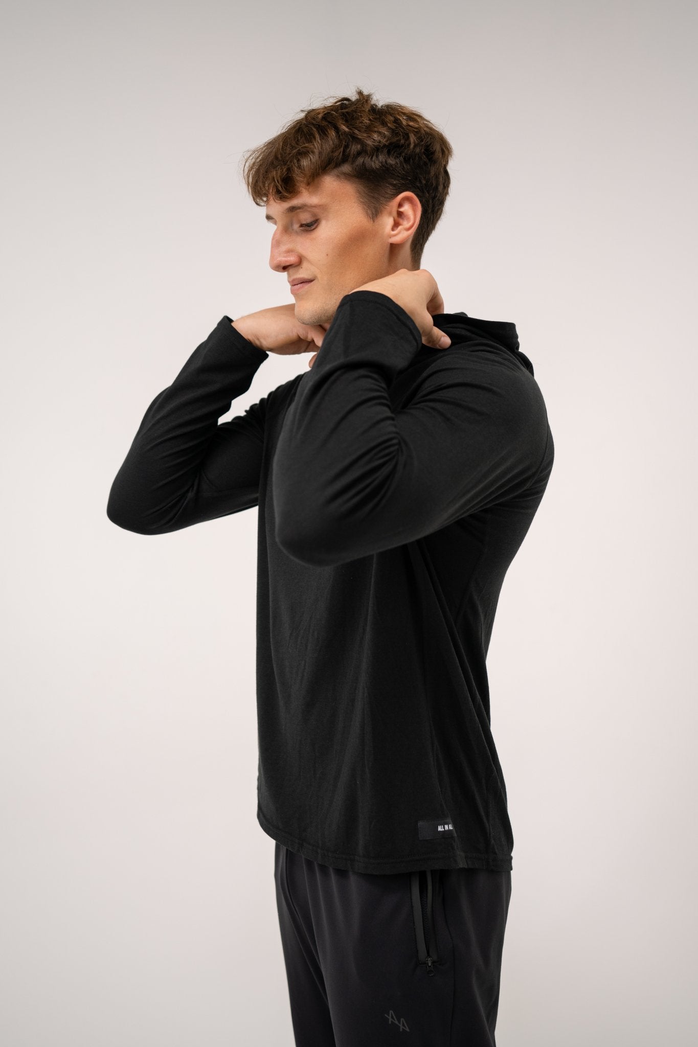 Male model wearing an ALL IN ALL black long-sleeve hoodie shirt against a white background