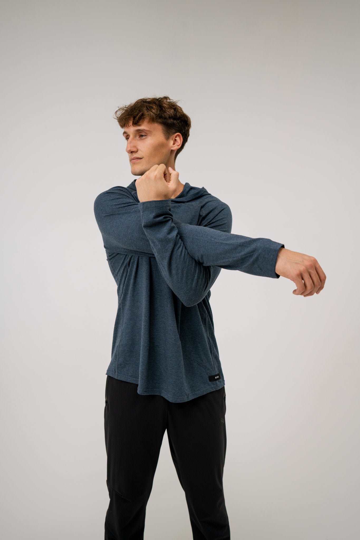 Male model wearing an ALL IN ALL heather blue long-sleeve hooded shirt and black ALL IN ALL joggers on a light background